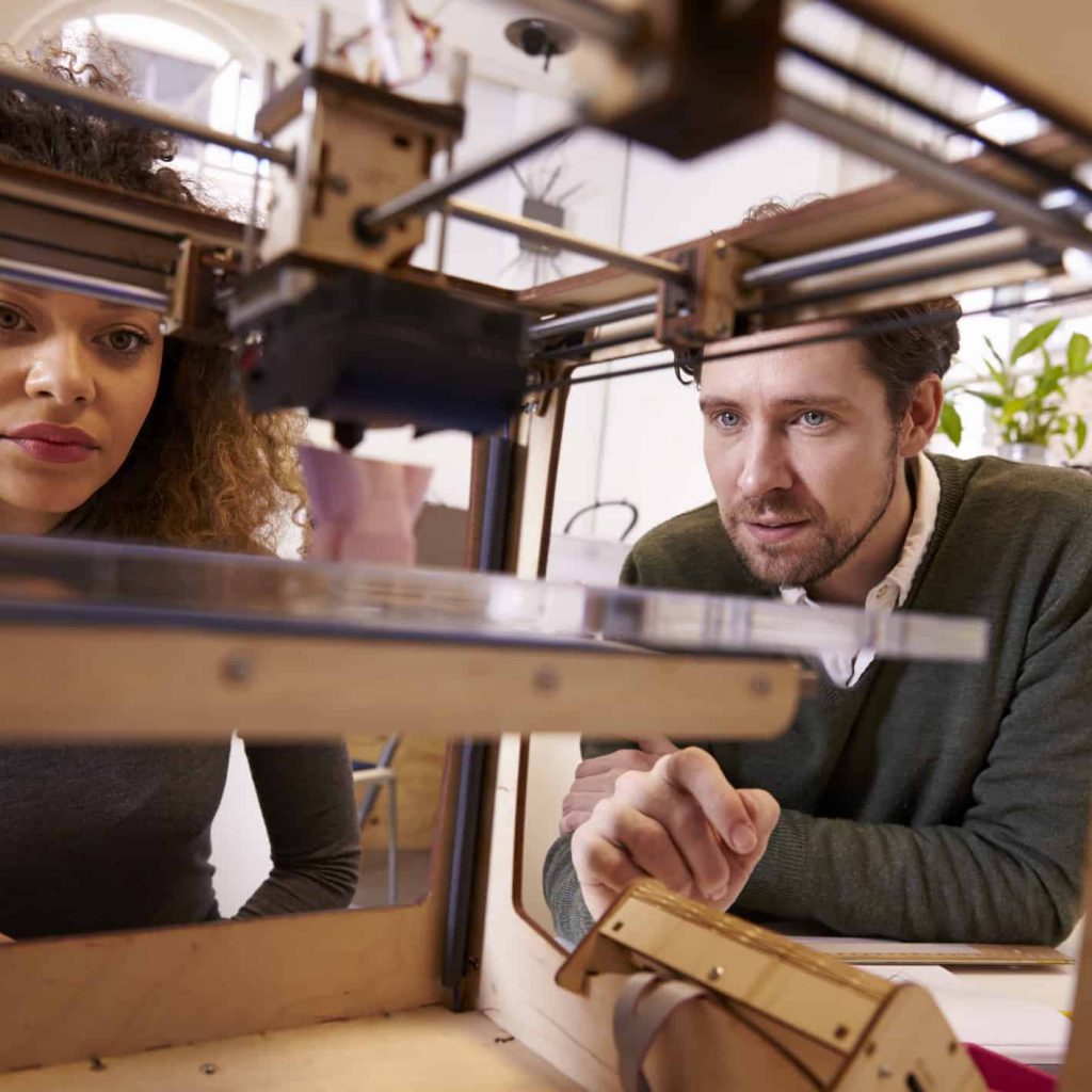 Two Designers Working With 3D Printer In Design Studio